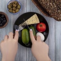 top view  woman cuts cheese with cucumbers  tomato  egg on a plate with black and green olives on gray background